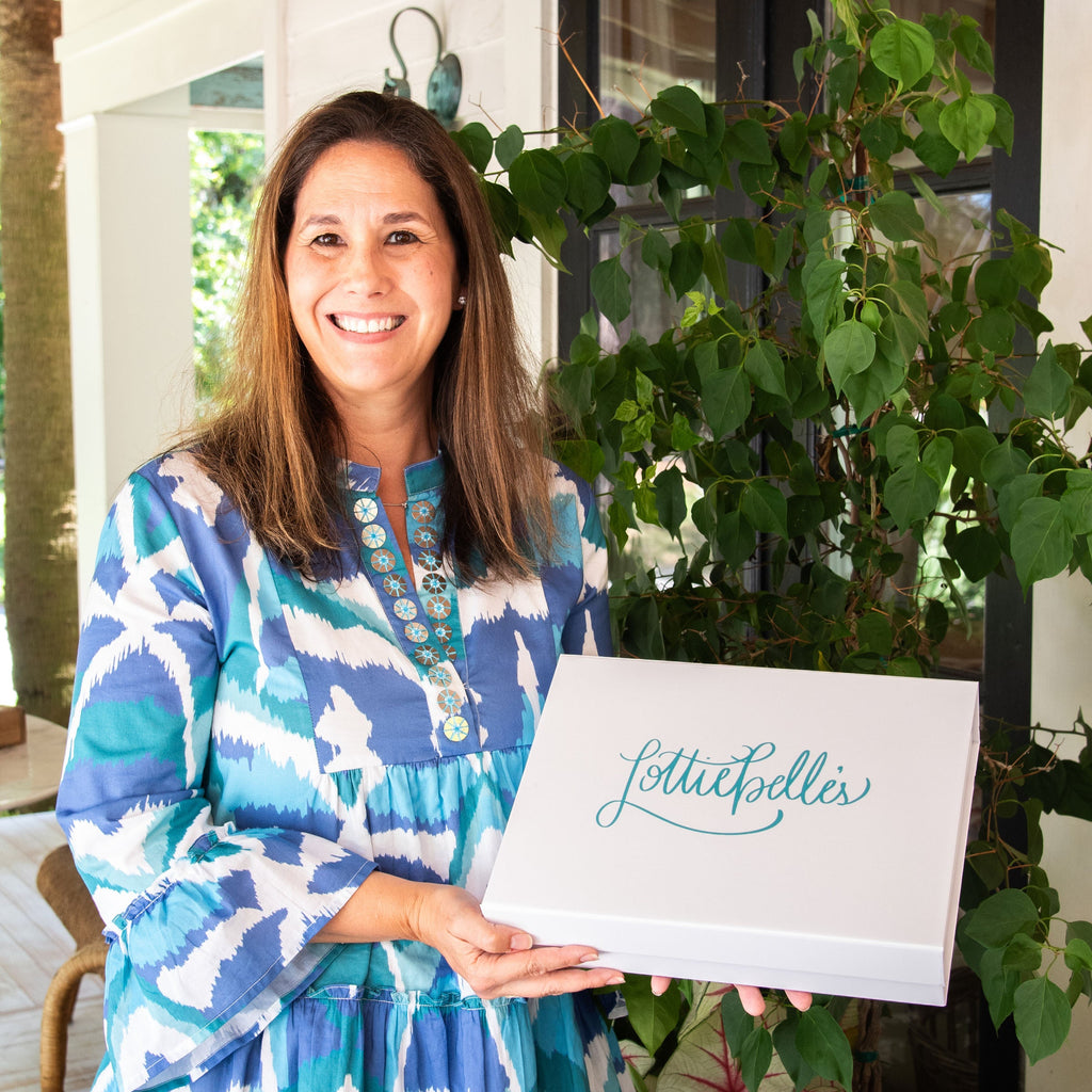Woman holding a gift box with 'Lottiebelle's in front of a house with plants.